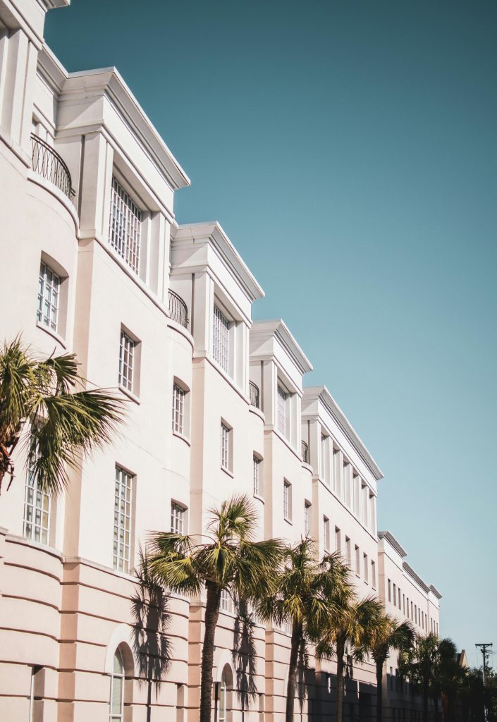 Façade moderne et lumineuse d’un bâtiment de l'hotel mahfouf, entourée de palmiers sous un ciel bleu clair.