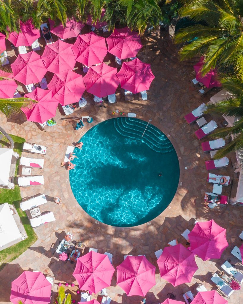 Vue aérienne d’une piscine de resort de luxe entourée de parasols roses vifs – idéale pour une escapade tropicale.